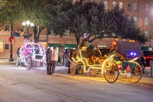 San Antonio, USA - October 31, 2023:  people enjoy to have a ride by night in the horse drawn carriage with colorful neon light in San Antonio at the river walk area.