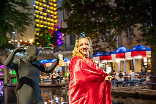 San Antonio, USA - October 31, 2023:  people at Halloween walk along the San Antonio River Walk with costumes by night with illuminated trees and restaurants.
