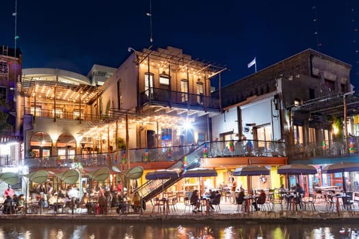 San Antonio, USA - October 31, 2023:  people enjoy the evening at the San Antonio River Walk with costumes by night and illuminated trees and restaurants.