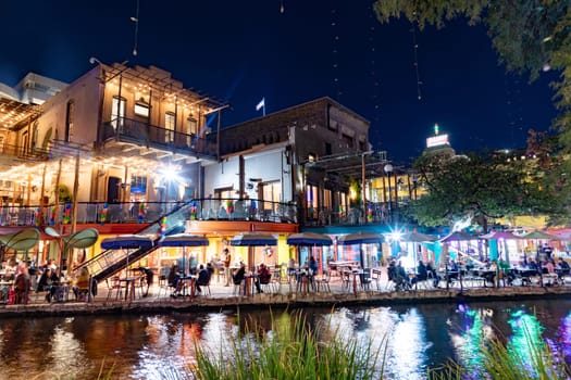 San Antonio, USA - October 31, 2023:  people enjoy the evening at the San Antonio River Walk with costumes by night and illuminated trees and restaurants.