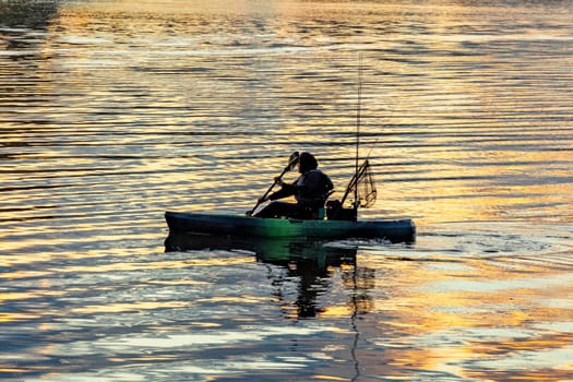 Austin, Texas - November 3, 2023: fisherman in early morning light fishes with his canoe at river colorado with golden sunrise reflections.