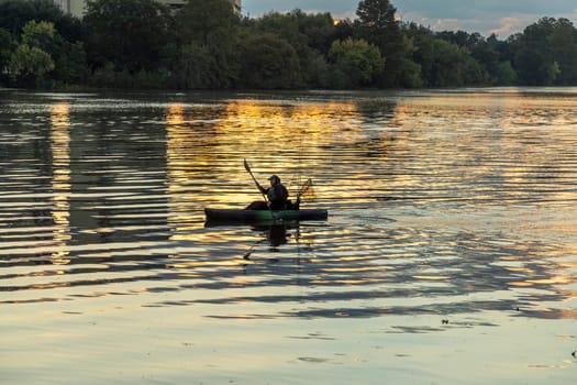 Austin, Texas - November 3, 2023: fisherman in early morning light fishes with his canoe at river colorado with golden sunrise reflections.