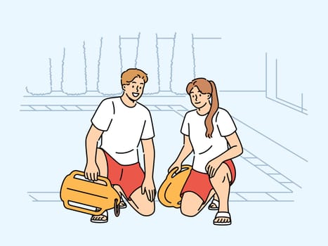 Pair of lifeguards sit by pool at hotel, holding swim training aids and keeping visitors safe. Smiling lifeguards or trainers working in fitness club urging people to visit swimming sports center
