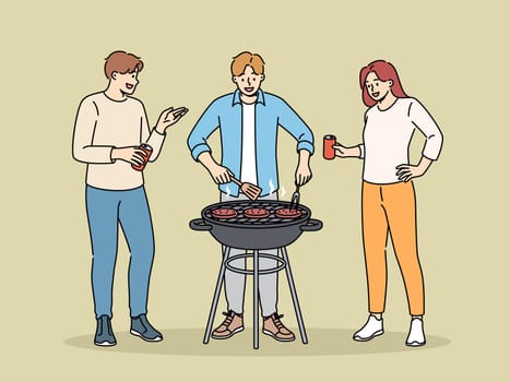 BBQ party with cheerful friends drinking beer and grilling meat on grill in park or in backyard of house. Happy people celebrating start of summer vacation and cooking beef meat on BBQ coals