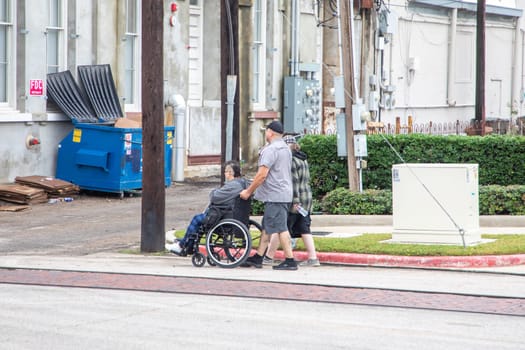 Galveston, USA - November 10, 2023: handicapped person at wheelchair with assistance by his family in the suburban area of Galveston, USA.
