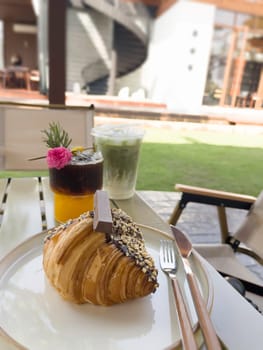 Single chocolate croissant and iced drink on table, stock photo