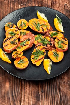 Homemade grilled sweet potato, batata with herbs on old rustic wooden table.