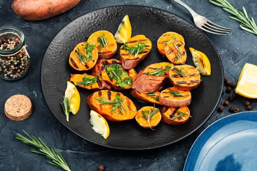 Homemade grilled sweet potato, batata with herbs on old rustic wooden table.