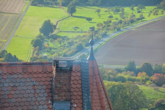 Smoking chimney on the roof of an old castle with a view of a green landscape from above