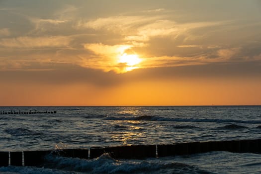Orang - red sunset over the ocean, with beach and breakwater made of wooden posts and seagulls