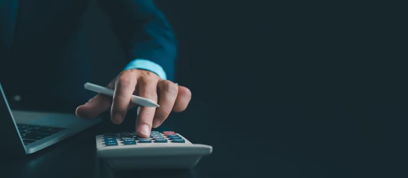 Businessman in black suit working on laptop computer and tablet and calculator, Hand Hands touch on tablet at office with dark background, Online working, Close up, Copy space.
