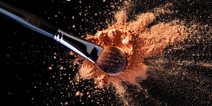 A makeup brush with scattered powder against a black background, highlighting cosmetic elegance.Great for makeup product display or artist portfolio.
