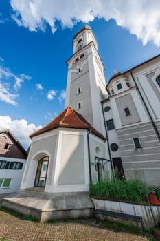 Wide-angle view of the Saint Andreas Church with bell tower and tower chapel in Nesselwang Bavaria from the northwest against a blue sky with clouds in summer 2023.