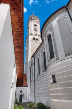 Wide-angle view of the bell tower with access to the tower chapel of the Saint Andreas Church in Nesselwang Bavaria from the west against a blue sky with small clouds in summer 2023.