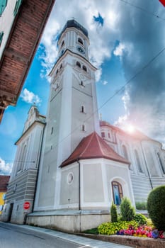 Extreme wide angle view north-side of the St. Andreas Church with bell tower in Nesselwang / Bavaria from north direction against blue cloudy sky in the summer of 2023.
