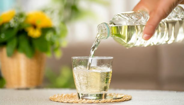 Close up the pouring purified fresh drink water from the bottle on table in living room