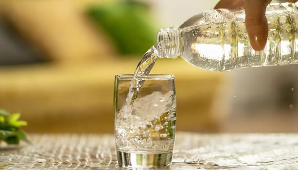 Close up the pouring purified fresh drink water from the bottle on table in living room