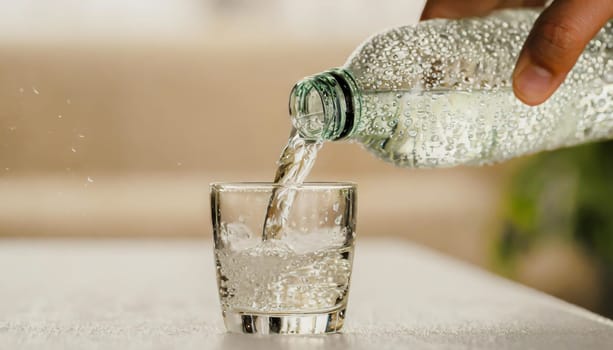 Close up the pouring purified fresh drink water from the bottle on table in living room