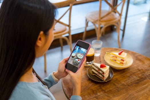 Woman take photo on the strawberry cake in coffee shop