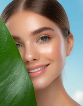 Portrait of young beautiful woman with healthy glow perfect smooth skin holds green tropical leaf, look into the hole of colored pink paper. Model with natural nude make up. Fashion, beauty, skincare