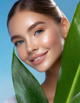 Portrait of young beautiful woman with healthy glow perfect smooth skin holds green tropical leaf, look into the hole of colored pink paper. Model with natural nude make up. Fashion, beauty, skincare
