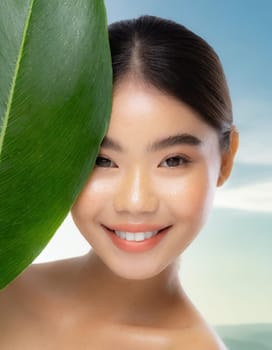 Portrait of young beautiful woman with healthy glow perfect smooth skin holds green tropical leaf, look into the hole of colored pink paper. Model with natural nude make up. Fashion, beauty, skincare