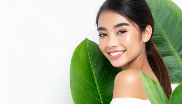 Portrait of young beautiful woman with healthy glow perfect smooth skin holds green tropical leaf. Model with natural nude make up. Gray background.