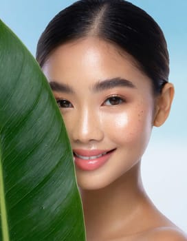 Portrait of young beautiful woman with healthy glow perfect smooth skin holds green tropical leaf, look into the hole of colored pink paper. Model with natural nude make up. Fashion, beauty, skincare