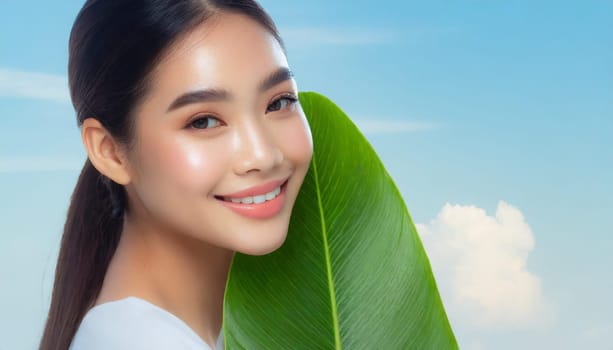 Portrait of young beautiful woman with healthy glow perfect smooth skin holds green tropical leaf. Model with natural nude make up. Gray background.