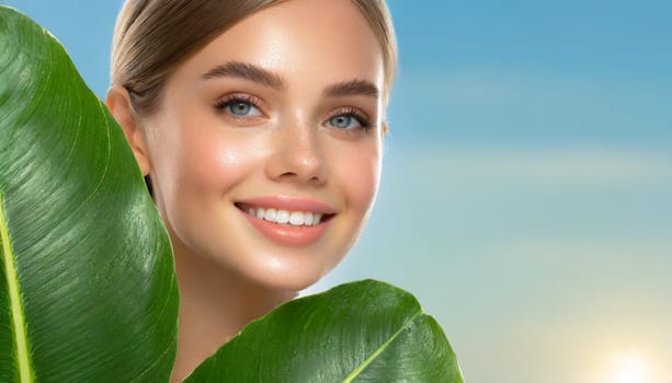 Portrait of young beautiful woman with healthy glow perfect smooth skin holds green tropical leaf. Model with natural nude make up. Gray background.