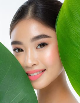 Portrait of young beautiful woman with healthy glow perfect smooth skin holds green tropical leaf. Model with natural nude make up. Gray background.