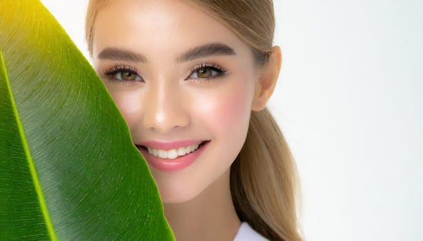 Portrait of young beautiful woman with healthy glow perfect smooth skin holds green tropical leaf. Model with natural nude make up. Gray background.