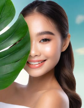 Portrait of young beautiful woman with healthy glow perfect smooth skin holds green tropical leaf. Model with natural nude make up. Gray background.