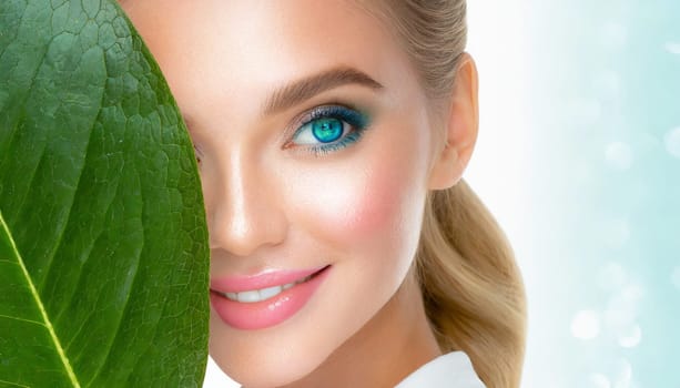 Portrait of young beautiful woman with healthy glow perfect smooth skin holds green tropical leaf. Model with natural nude make up. Gray background.