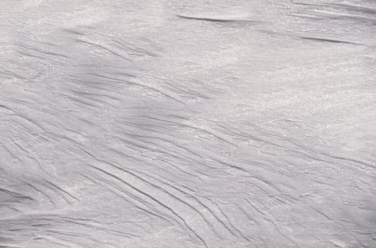 Snowy gray background with glitter and natural streaks from the wind during the day close-up view from above