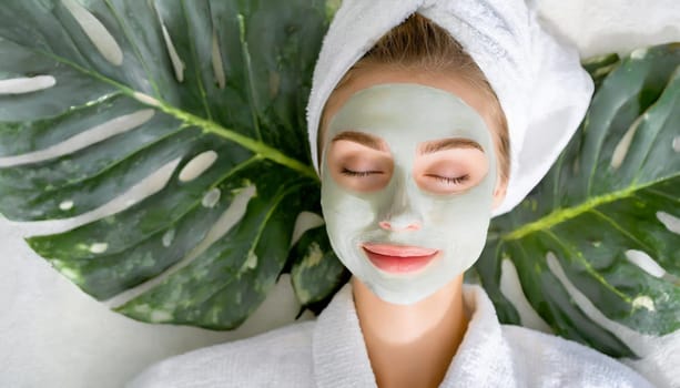 Skin care. Cheerful attractive caucasian female with clay mask on face and cucumber slices in hands against blue background getting beauty treatment. Spa concept with copy space