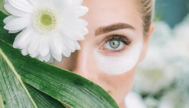 Portrait of beautiful woman with healthy glow perfect smooth skin holds tropical leaf, look into the hole of green paper. Young girl enjoys cream facial mask. Fashion, beauty, skincare concept.