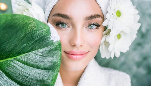 Portrait of beautiful woman with healthy glow perfect smooth skin holds tropical leaf, look into the hole of green paper. Young girl enjoys cream facial mask. Fashion, beauty, skincare concept.