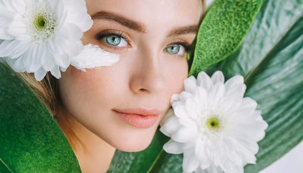Portrait of beautiful woman with healthy glow perfect smooth skin holds tropical leaf, look into the hole of green paper. Young girl enjoys cream facial mask. Fashion, beauty, skincare concept.