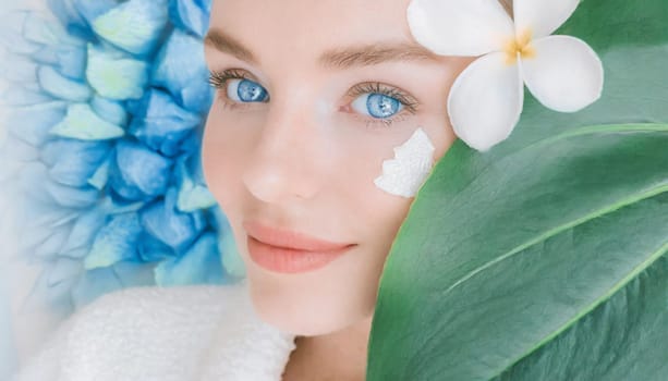 Portrait of beautiful woman with healthy glow perfect smooth skin holds tropical leaf, look into the hole of green paper. Young girl enjoys cream facial mask. Fashion, beauty, skincare concept.