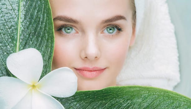 Portrait of beautiful woman with healthy glow perfect smooth skin holds tropical leaf, look into the hole of green paper. Young girl enjoys cream facial mask. Fashion, beauty, skincare concept.