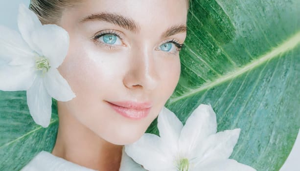 Portrait of beautiful woman with healthy glow perfect smooth skin holds tropical leaf, look into the hole of green paper. Young girl enjoys cream facial mask. Fashion, beauty, skincare concept.