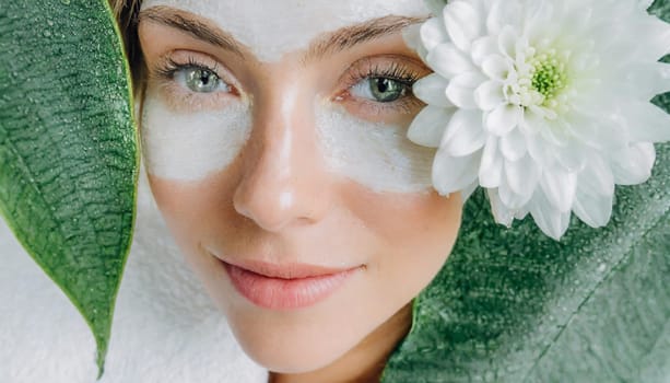 Portrait of beautiful woman with healthy glow perfect smooth skin holds tropical leaf, look into the hole of green paper. Young girl enjoys cream facial mask. Fashion, beauty, skincare concept.