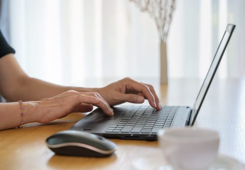 Woman using laptop computer while typing on her notebook while working online from home.