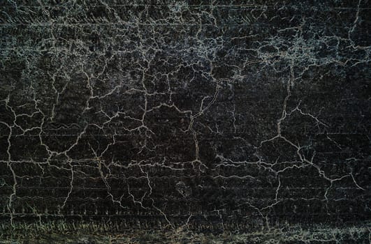 Grunge textured background with dirty surface and interlacing cracks on a black background