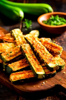 Crispy parmesan zucchini fries on a wooden board, served with a fresh parsley garnish.