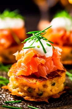 Elegant canapes with smoked salmon and cream, garnished with fresh garlic on a dark plate.