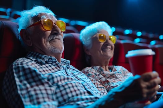 An elderly couple watches a movie in a cinema wearing glasses - a refreshing take on active aging. Copy space.
