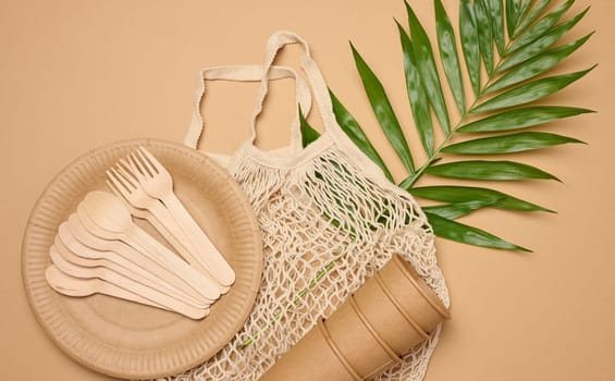 Paper plates and cups, wooden spoons and forks on a beige background, top view