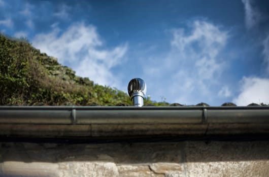 Wind-rolling home cowl with rain gutter. Blue sky background